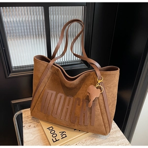 Detail view of brown suede tote bag with MORCAI embossed text and elephant charm