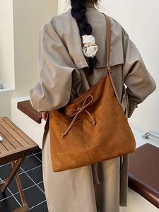 Retro brown suede tote bag with leather strap and bow detail on a minimalist trench coat