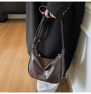Chic dark brown hobo bag worn by a model in a black coat for a stylish commuter look