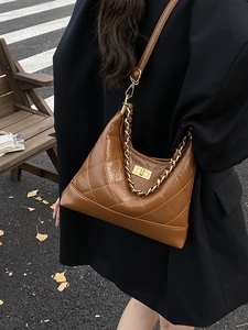 Sac hobo marron matelassé en cuir avec chaîne dorée porté par un mannequin en extérieur