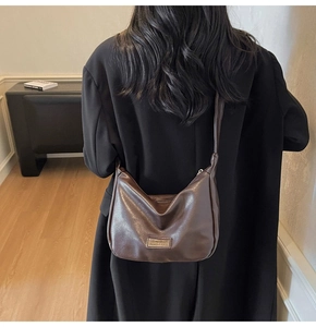 Detail of soft dark brown synthetic leather texture and metallic logo on the crossbody bag