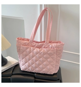 Detail of light pink quilted nylon tote bag with rhombus pattern on a black leather bench
