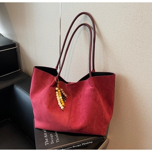 Detail of red suede tote bag with decorative tassel on dark design books