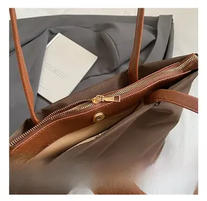 Detail view of the brown tote bag featuring gold metal zipper and magnetic closure