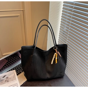 Detail of black suede tote bag with retro wooden beaded charm on a leather desk
