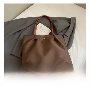 Detail showing deep brown nylon tote bag with leather handles and magnetic metal buckle