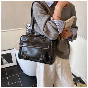 Detail of black faux leather tote bag featuring metal buckles and zippered pocket