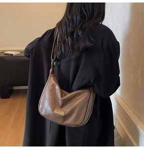 Brown leather Hobo bag featuring wavy pleats and adjustable strap on a black blazer