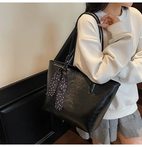 Detail of black leather tote bag with polka dot scarf on handle for daily commute