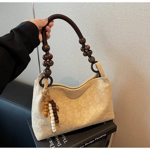 Detail of beige quilted shoulder bag with unique wooden bead rope handle and charm