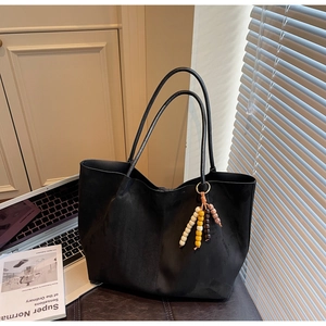 Detail of black suede tote bag with colorful beaded tassel in a lifestyle office setting