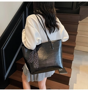 Detail of a large black tote bag with glossy leather texture and polka dot scarf handle