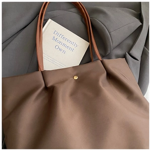 Detail of high-capacity brown tote bag featuring a gold snap closure and soft shoulder strap