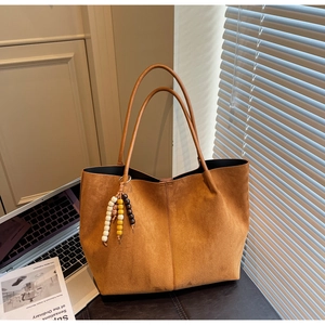 Close-up of brown suede tote bag featuring a decorative beaded charm and smooth texture
