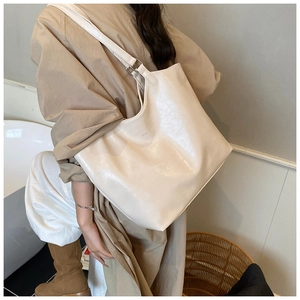 Detail of a large cream-colored matte leather tote bag with a metallic buckle on strap