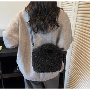 Close-up of black fuzzy plush shoulder bag with leather strap worn by a model in a knit sweater