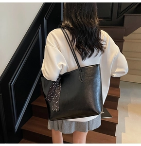 Detailed close-up of a black leather tote bag with a polka dot scarf on a model