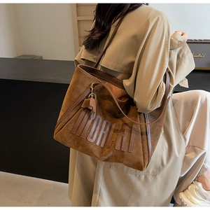 Detail of a brown suede tote bag featuring a 3D MORCHI letter patch and leather handles