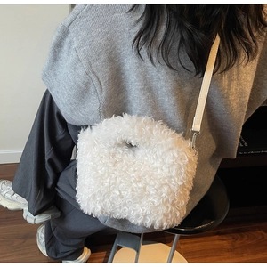 Close-up of fluffy white faux fur crossbody bag with leather strap on a grey sweater