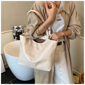 Detail of a large cream tote bag in shiny synthetic leather on a beige trench coat