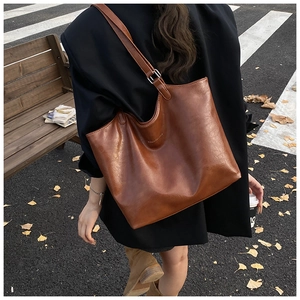 Brown vintage leather tote bag styled on model with long strap in autumn street setting