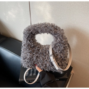 Close-up of grey curly plush handbag with adjustable beige leather strap on book