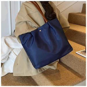 Navy blue nylon tote bag with brown leather handles worn by a model in a trench coat