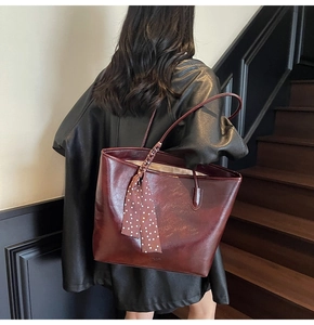Detail view of a burgundy oil-wax tote bag with a polka dot scarf on a model