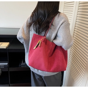 Detail of a deep red suede tote bag with a colorful ethnic style beaded charm on shoulder