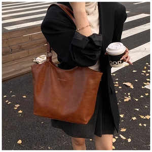 Brown leather tote bag worn by a model in an urban autumn street style setting