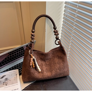 Detail of dark brown suede handbag featuring quilted texture and wooden bead handle