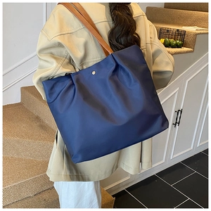 Detail of navy nylon tote bag with brown leather handles and golden magnetic closure