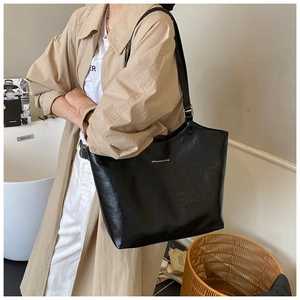 Detailed view of black faux leather tote bag with white logo and natural wrinkled texture