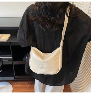 Close-up of beige hobo dumpling bag with brand patch and zipper detail shown on model