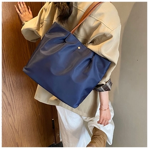 Close-up of navy blue tote bag with brown leather straps and gold metal clasp detail