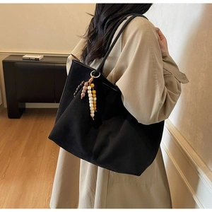 Detail of black suede tote bag with colorful wooden beaded tassel and shoulder strap