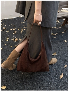 Detail der dunkelbraunen Wildleder-Hobo-Tasche auf herbstlicher Straße mit Ginkgo