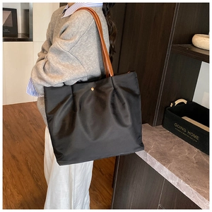 Detail of black tote bag with pleated edge, golden hardware, and brown leather strap
