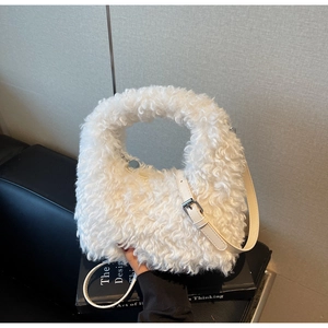 Close-up of white plush crossbody bag on a book, showing soft faux fur texture and zipper