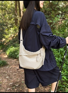 Detail of light beige crescent crossbody bag with braided zipper pullers in forest setting