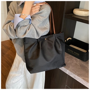 Detail of black nylon tote bag featuring gold button closure and brown leather handles