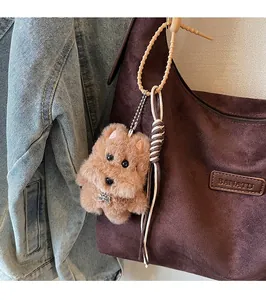 Close-up of a brown plush puppy charm with TOP DOG tag on a suede tote bag