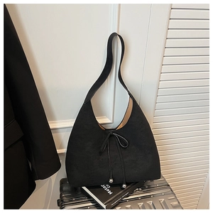 Detail of black suede crescent bag with drawstring bow on a silver suitcase