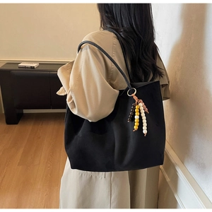 Detail view of black suede tote bag with artistic wooden bead charm on shoulder strap