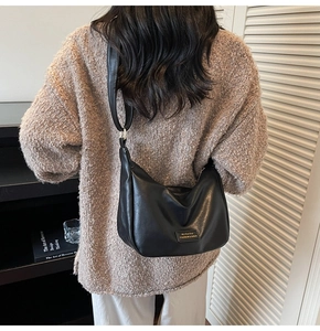 Detail of a black PU leather dumpling bag with wide strap on a model in a cozy interior