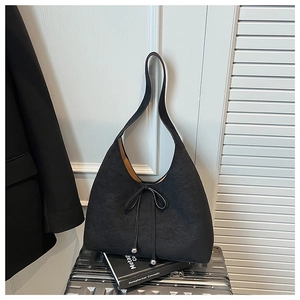 Close-up of black suede hobo bag featuring bow detail and metallic beads on soft strap