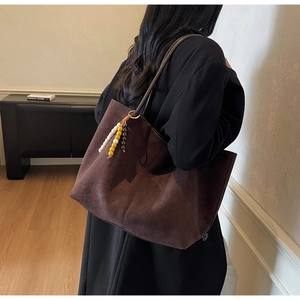 Detail of a large brown suede tote bag with a three-color beaded charm on model