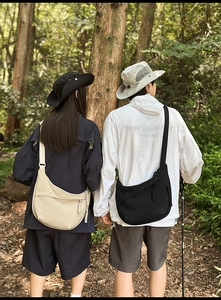 Outdoor forest scene showing nylon crossbody messenger bags with woven zip pulls
