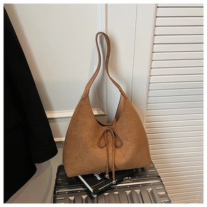 Close-up of caramel suede hobo bag with drawstring bow detail on a vintage suitcase
