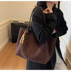 Detail of dark brown suede tote bag featuring a colorful wooden bead tassel and slim strap